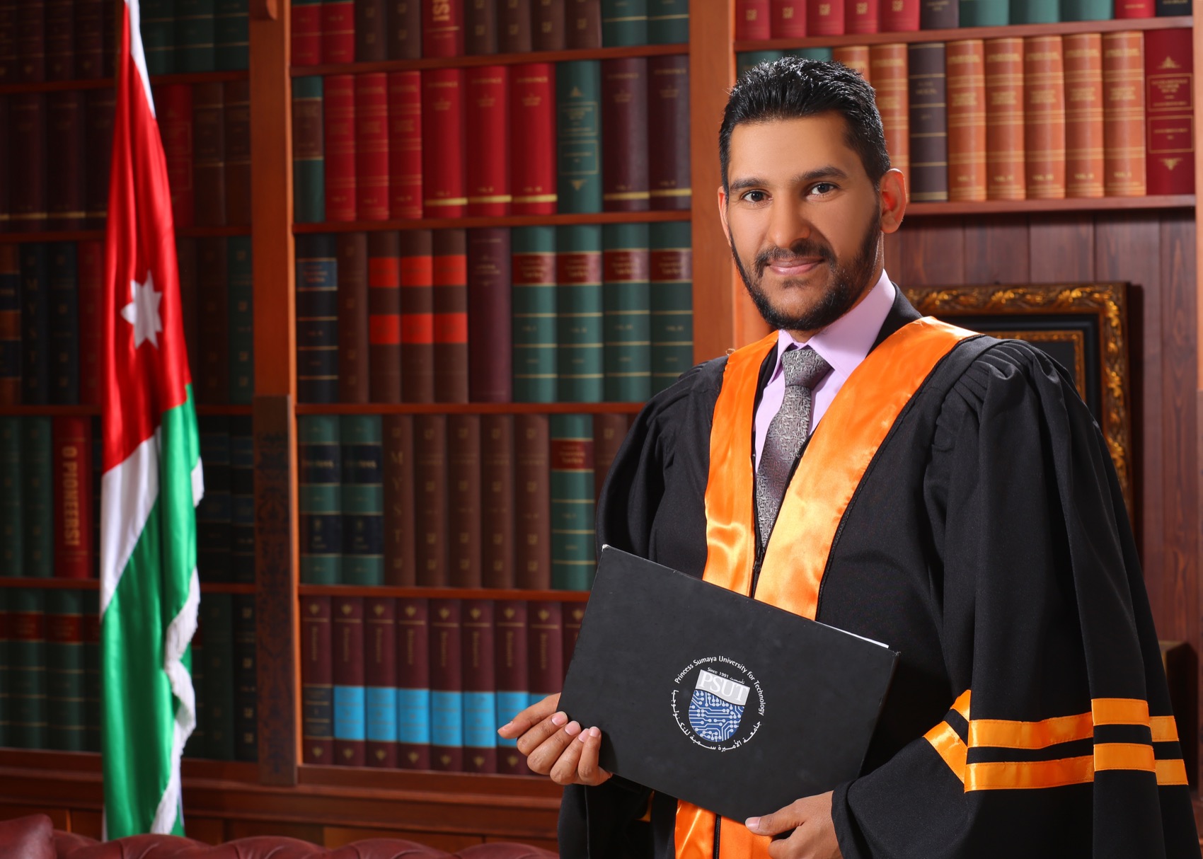 Muayyad Alsadi in academic dress, the Jordanian flag beside him.
